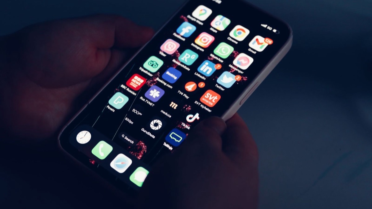 A person's hands holding a smartphone and tapping app icons on the touchscreen