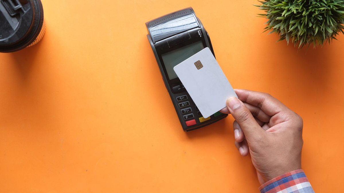A hand holding a blank chip card above a card payment terminal on an orange background