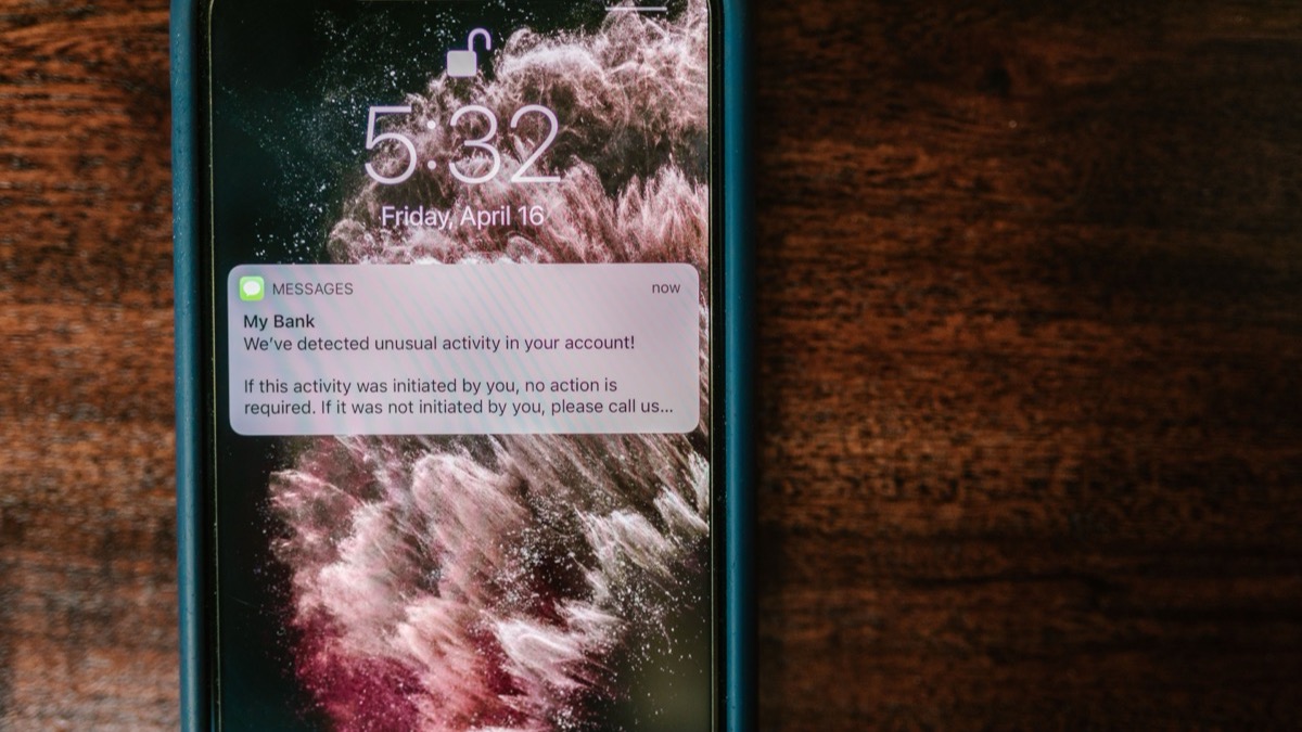An iPhone on a wooden table showing a lock screen banner from a bank reading that unusual activity was detected in the account