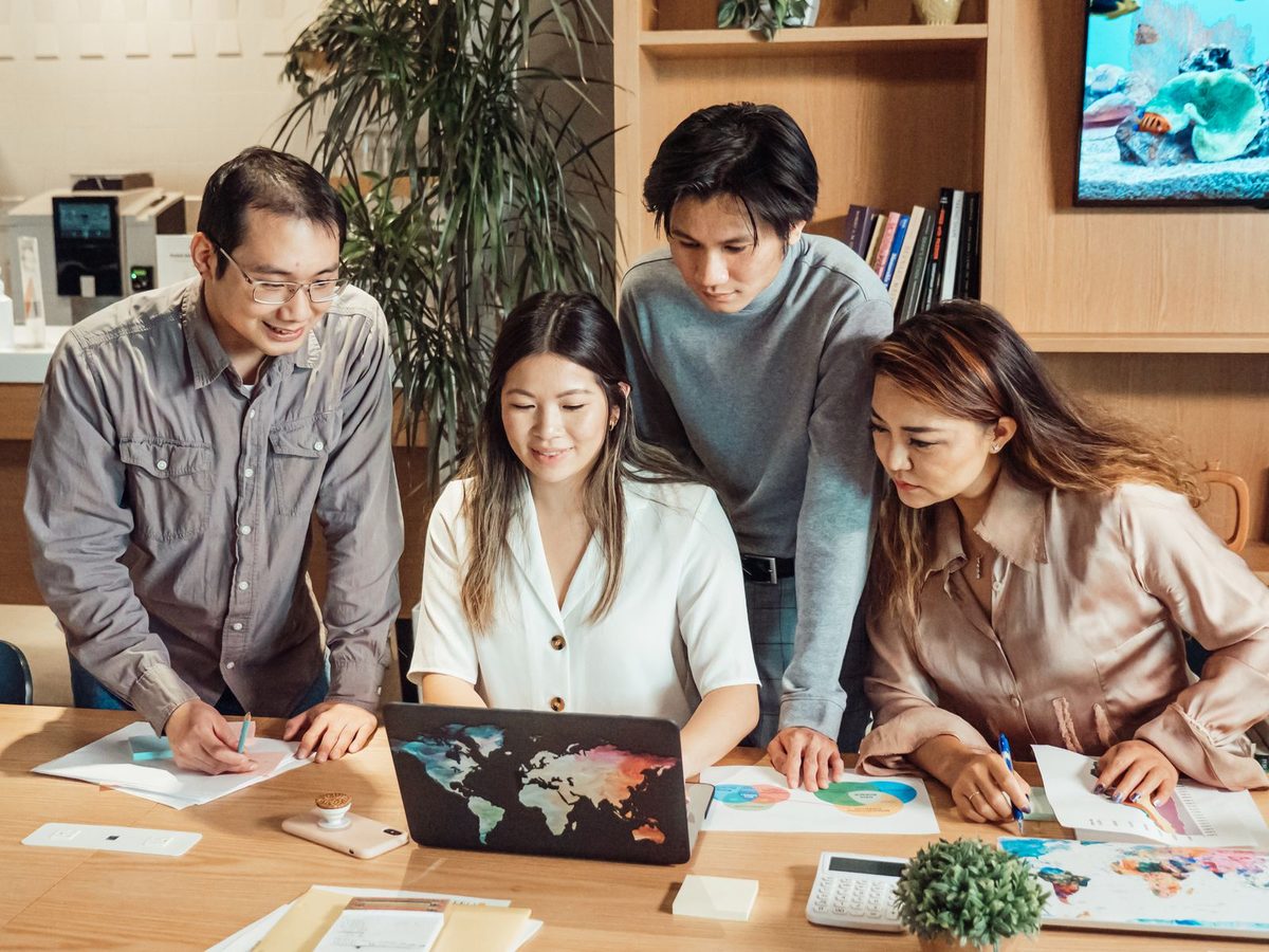 A team of four colleagues in an office reviewing printed documents and charts around a laptop